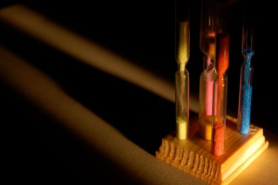 Mehrere Sanduhren mit buntem Sand in einem Holzständer im Streiflicht