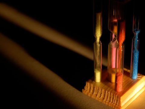 Mehrere Sanduhren mit buntem Sand in einem Holzständer im Streiflicht