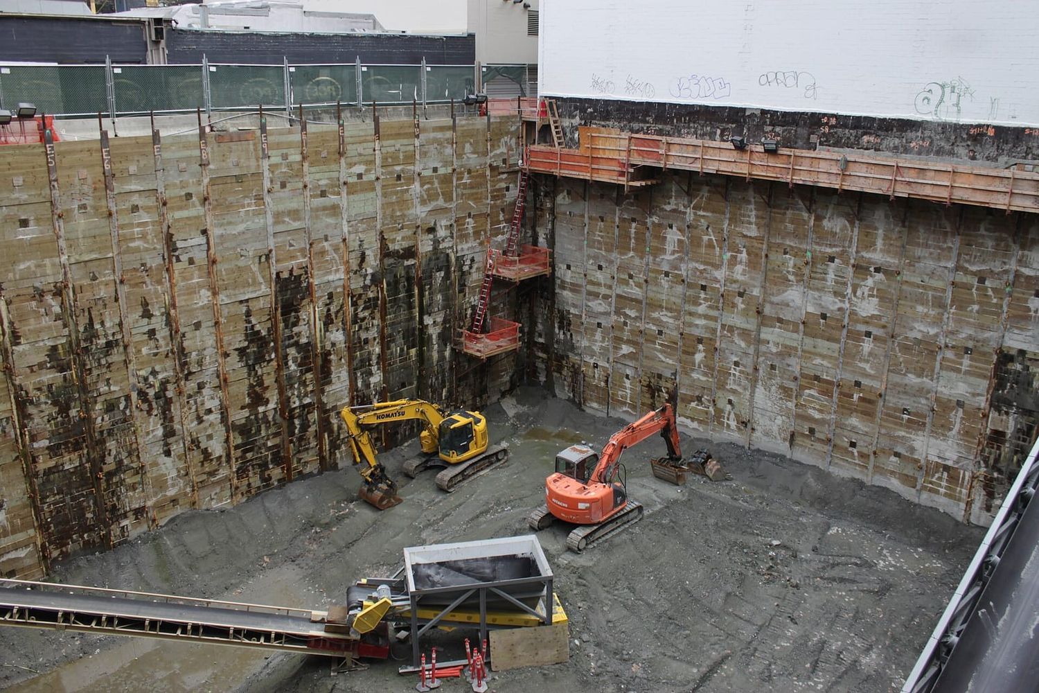 Tiefe Baugrube mit zwei Baggern und Förderband auf einer stillstehenden Baustelle