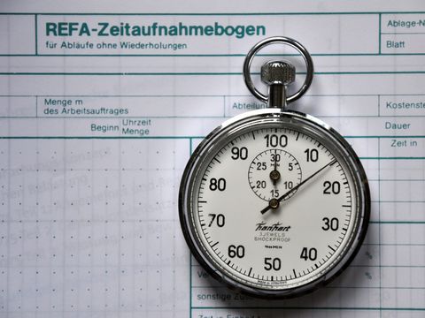Mechanische Stoppuhr auf einem Zeitaufnahmebogen mit Spalten für Dauer und Kostenstelle