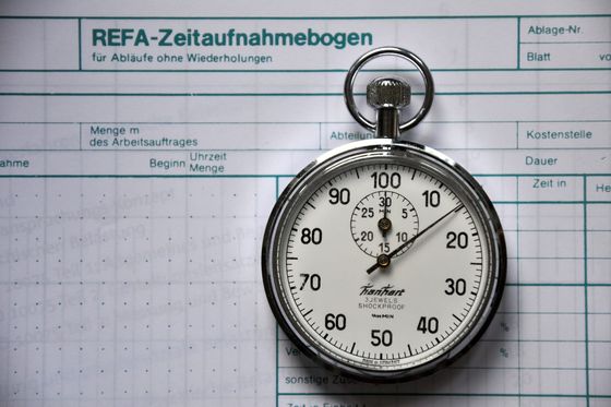 Mechanische Stoppuhr auf einem Zeitaufnahmebogen mit Spalten für Dauer und Kostenstelle