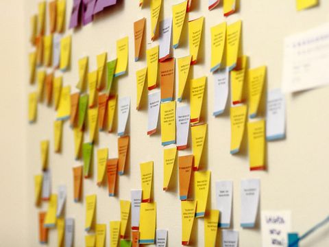 Viele bedruckte Haftnotizen in Gelb, Orange und Weiß an einer Bürowand