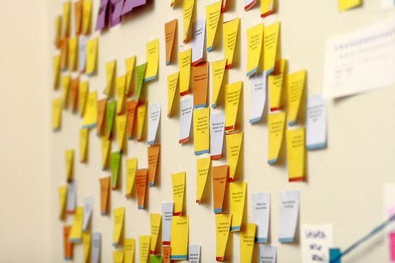Viele bedruckte Haftnotizen in Gelb, Orange und Weiß an einer Bürowand